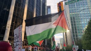 The flag of Palestine, consisting of black, white and green stripes bordered by a red triangle, is flown during a protest down Burrard Street in Vancouver. Signs carried by protestors read 'end the occupation'