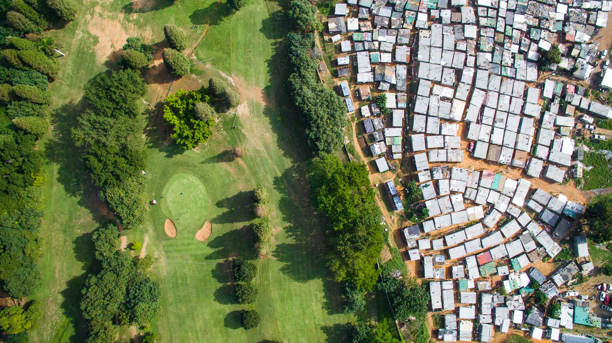 Papwa Sewgolum Golf Course is located along the lush green slopes of the Umgeni River in Durban. Almost unbelievably, a sprawling informal settlement exists just meters from the tee for the 6 hole. A low-slung concrete fence separates the tin shacks from the carefully manicured fairways. In a twist of irony, the golf course is named after an apartheid-era golfer of Indian descent, named Sewsunker “Papwa” Sewgolum. Papwa Sewgolum was an excellent self-taught golfer, with no formal schooling.